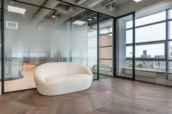 Moderne wachtruimte met een beige designbank, glazen wanden en uitzicht op de skyline vanaf de Joop Geesinkweg.